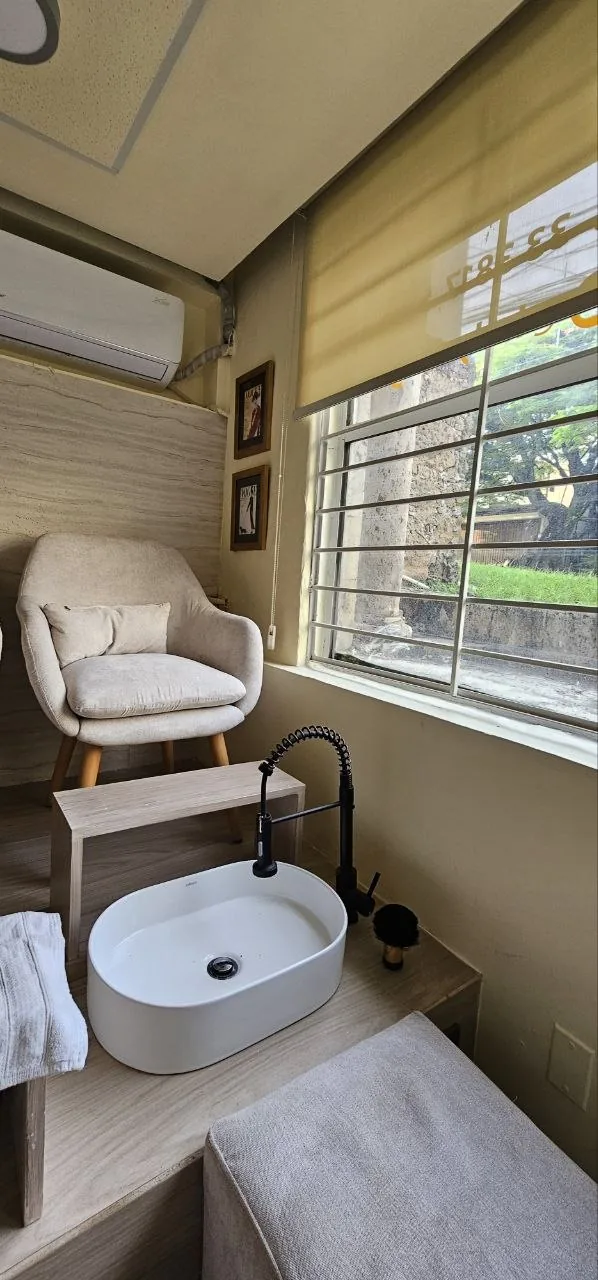 Estación de pedicure spa con lavabo blanco, sillón beige y ventana con vista a jardín en Holy Chic, Guadalajara